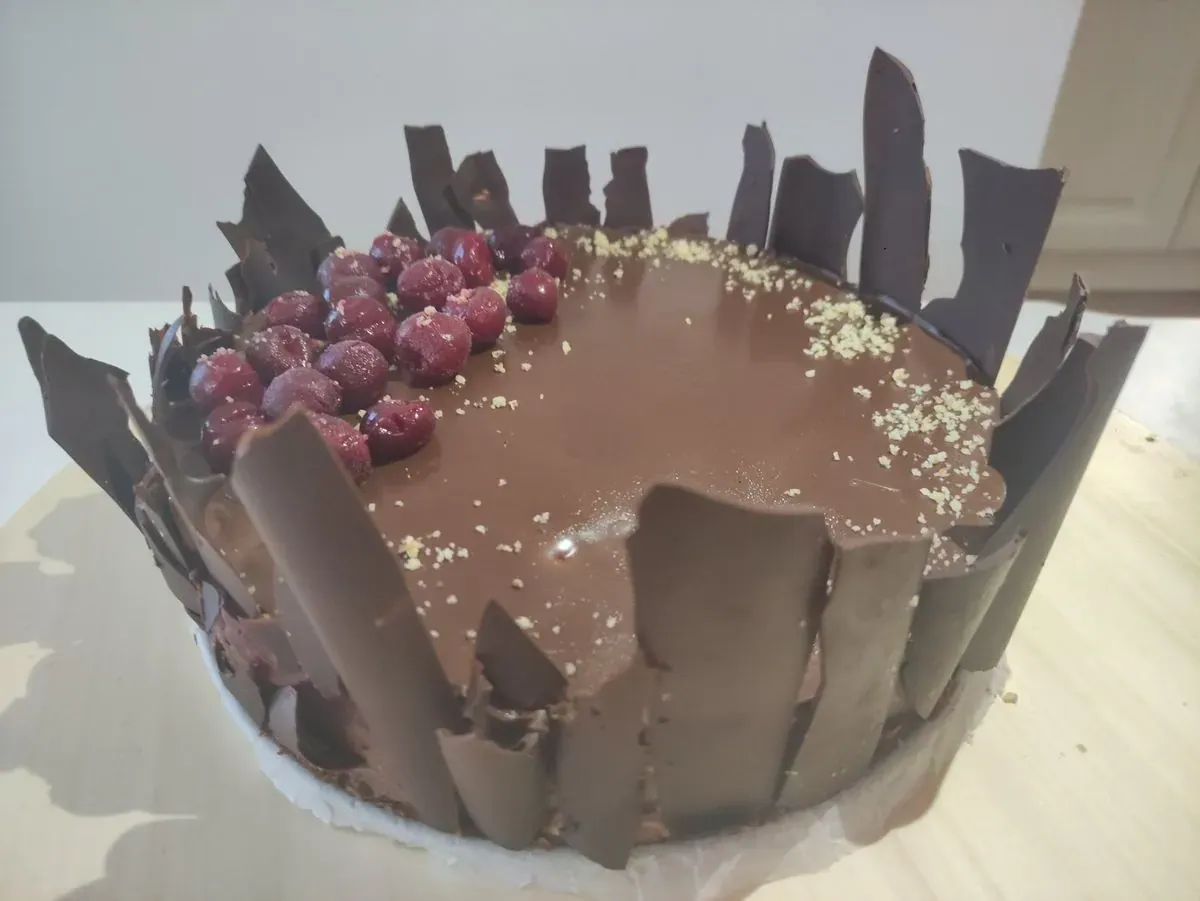 Čokoladna torta sa glazurom, višnjama i čokoladnim listićima oko ivice