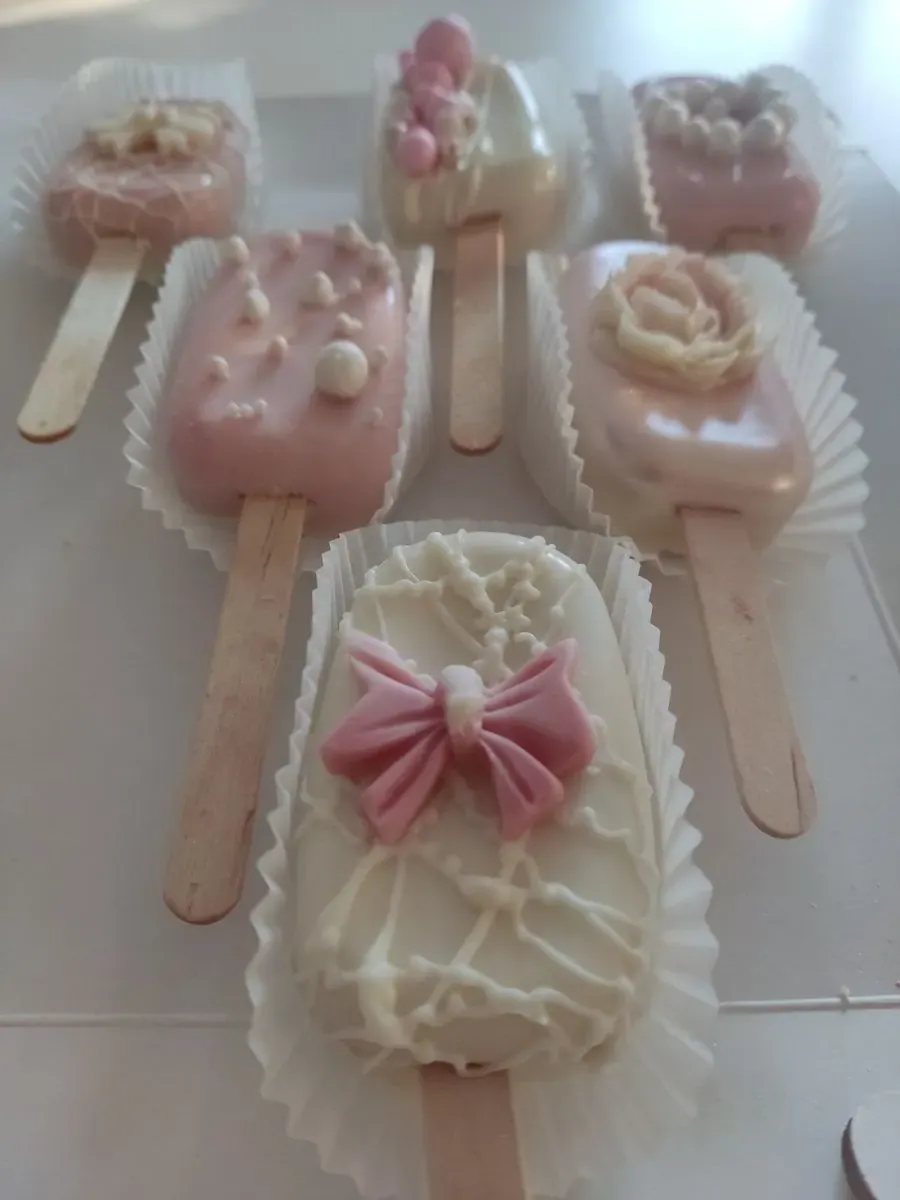 Pops sladoledi prelivani roze i belom čokoladom, ukrašeni mašnom, perlicama i čokoladnim cvetom