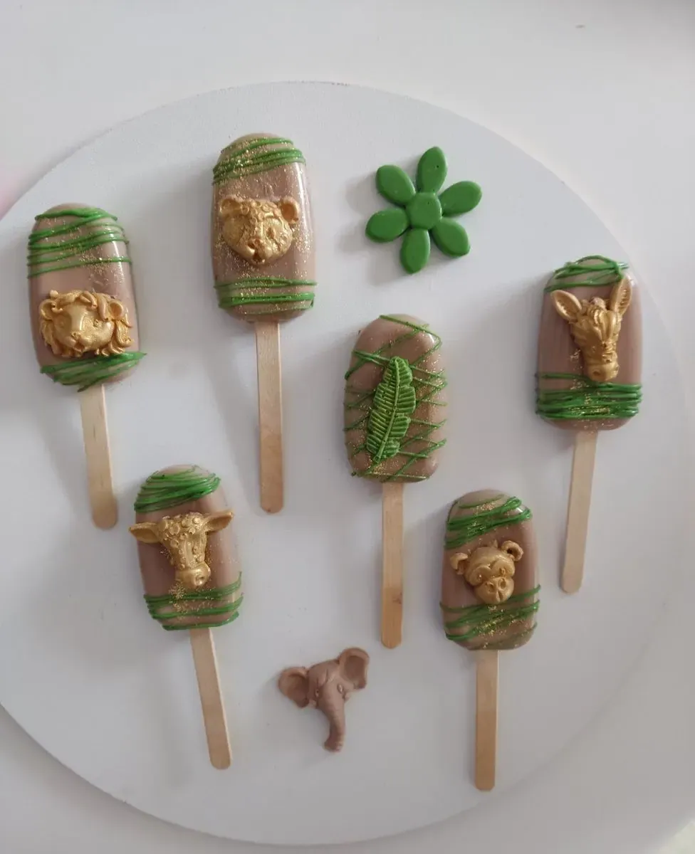Čokoladni pops sladoledi sa zlatnim figurama životinja i zelenim cvetom na beloj tacni