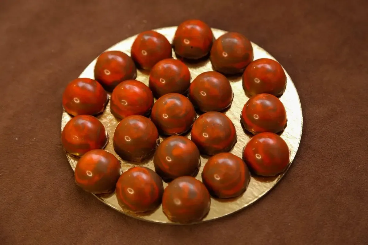 Čokoladne praline narandžasto-crvenih tonova poređane na zlatnoj tacni