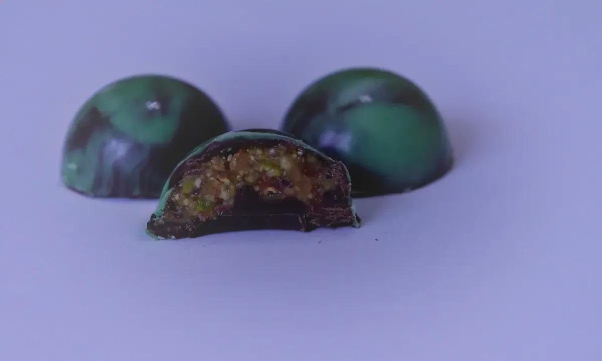 Zelene čokoladne praline, jedna presečena da se vidi punjenje od pistaća