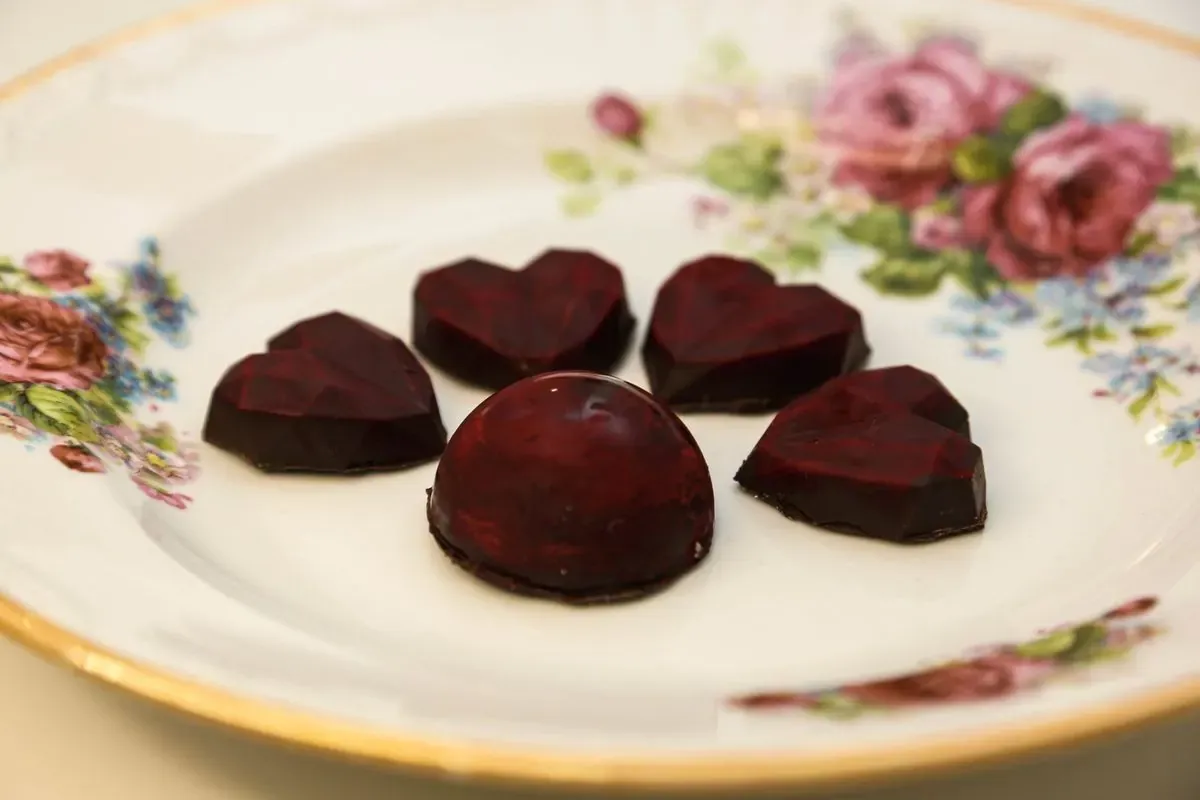 Tamne čokoladne praline u obliku srca i polulopte na porcelanskom tanjiru sa cvetnim motivom