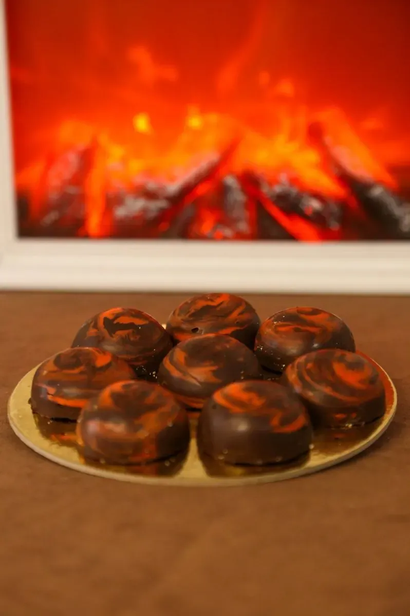 Tamne čokoladne praline sa narandžastim šarama na zlatnoj tacni